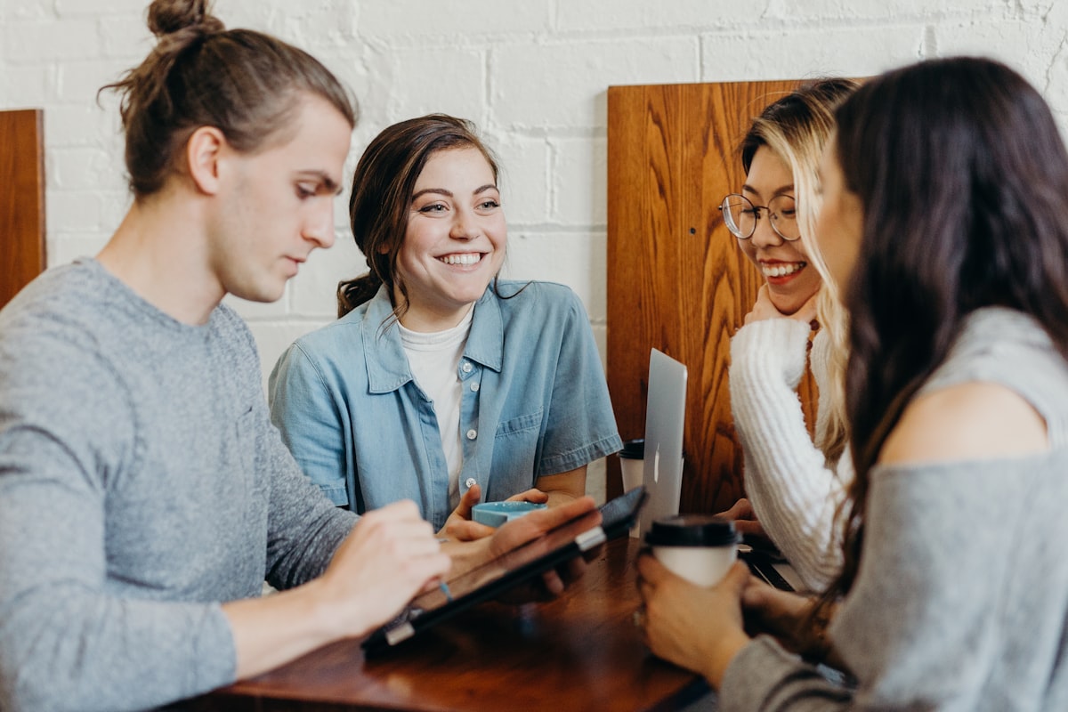 Grupo de amigos sorrindo e conversando ao redor de uma mesa, representando uma indicação entre conhecidos